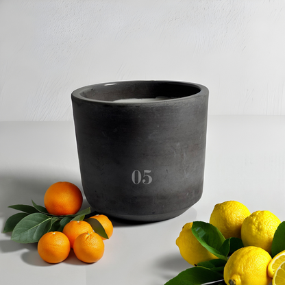 05 Zara candle on a glossy white surface surrounded by bergamot and lemons